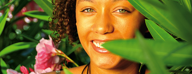 Lächelnde Frau zwischen grünen Blättern und rosa Blüten in einer tropischen Umgebung während einer Sprachreise in Le Gosier auf Guadeloupe